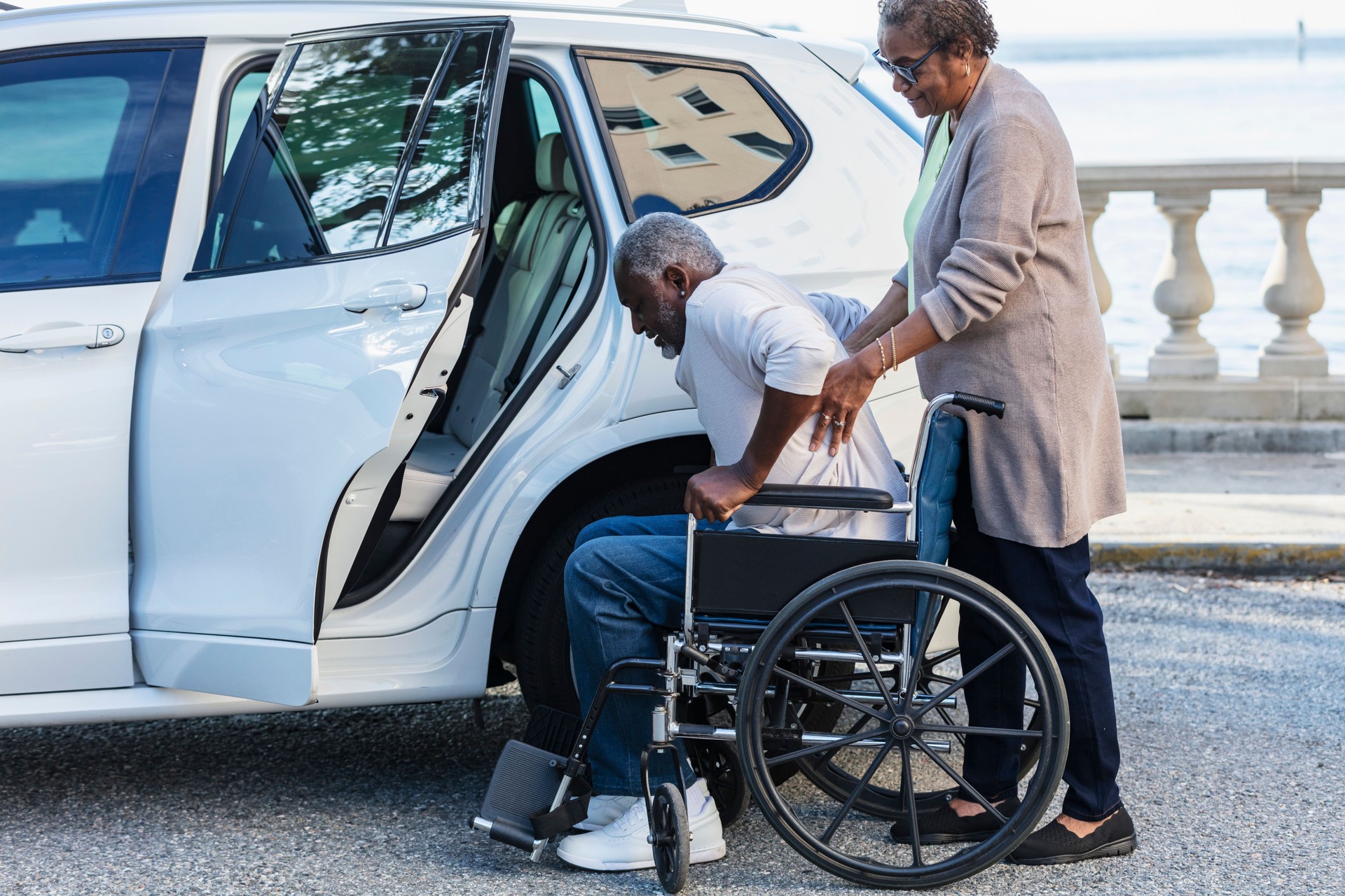 Senior man moving from wheelchair to car, wife helping